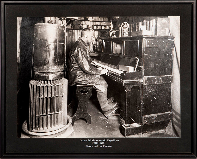 Classic Herbert Ponting photograph from Captain Scott's Terra Nova expedition (1910-1913), showing Cecil Meares sitting at the pianola in The Hut.