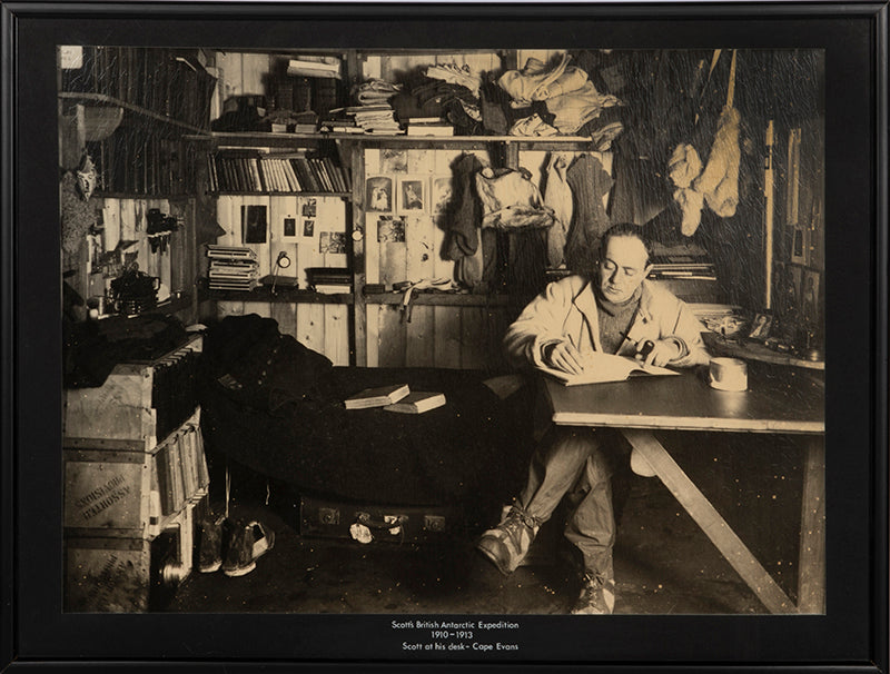 Classic Herbert Ponting photograph from Captain Scott's Terra Nova expedition (1910-1913), showing Captain Scott at his desk in the Hut at Cape Evans.