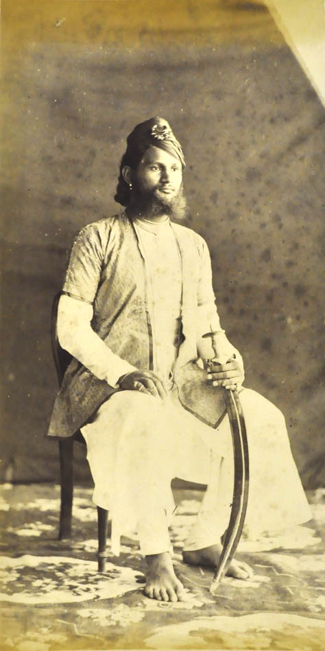 An albumen print with good tonal range, showing a seated man with a talwar, a curved Indian sword.