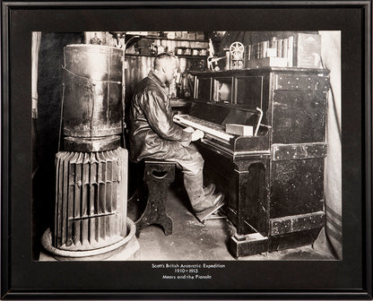 Classic Herbert Ponting photograph from Captain Scott's Terra Nova expedition (1910-1913), showing Cecil Meares sitting at the pianola in The Hut.