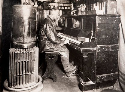 Classic Herbert Ponting photograph from Captain Scott's Terra Nova expedition (1910-1913), showing Cecil Meares sitting at the pianola in The Hut.