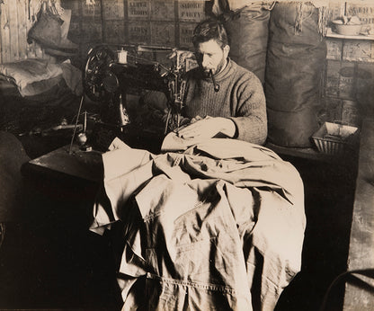 Classic Herbert Ponting photograph from Captain Scott's Terra Nova expedition (1910-1913), showing Petty Officer Edgar Evans sewing a tent in the Hut.