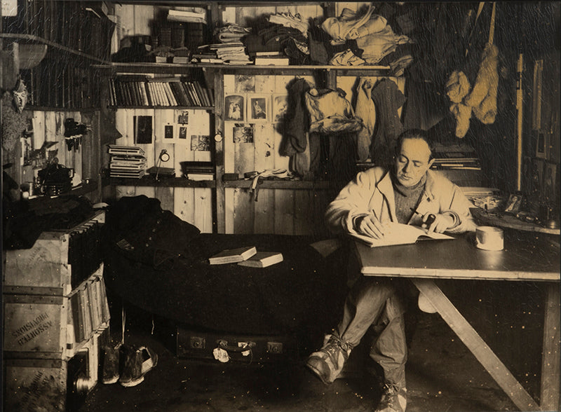 Classic Herbert Ponting photograph from Captain Scott's Terra Nova expedition (1910-1913), showing Captain Scott at his desk in the Hut at Cape Evans.
